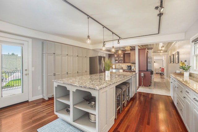 kitchen featuring dark hardwood / wood-style flooring, hanging light fixtures, a kitchen island, rail lighting, and stainless steel fridge