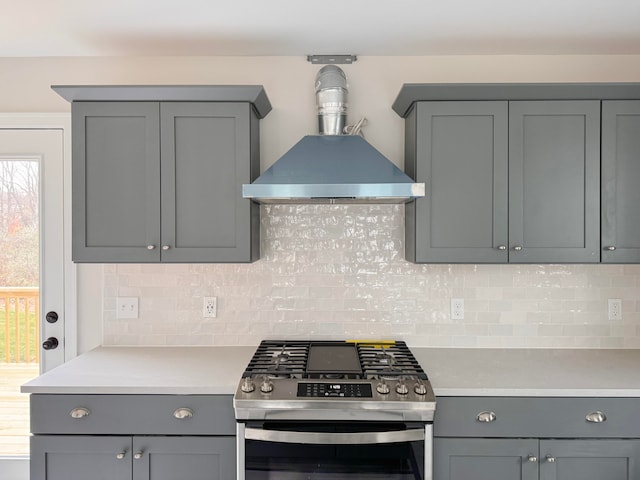 kitchen featuring backsplash, stainless steel range with gas stovetop, gray cabinets, and wall chimney range hood