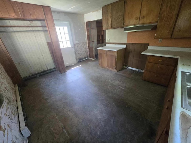 kitchen with concrete flooring, light countertops, brown cabinets, and under cabinet range hood