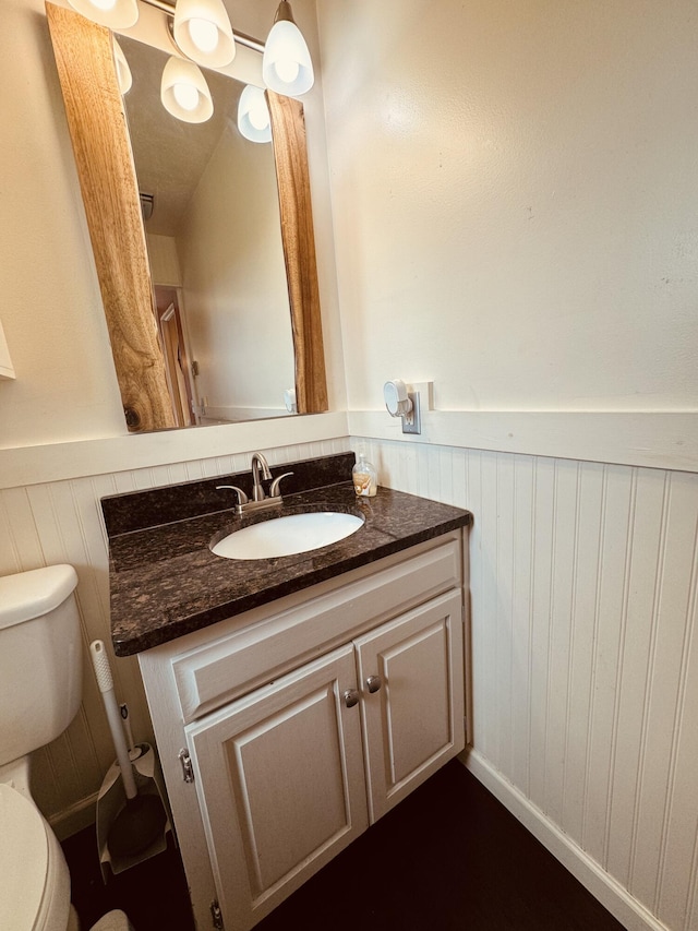 bathroom with vanity, toilet, and wood walls