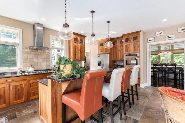 kitchen featuring stainless steel appliances, a kitchen island, wall chimney range hood, and a healthy amount of sunlight