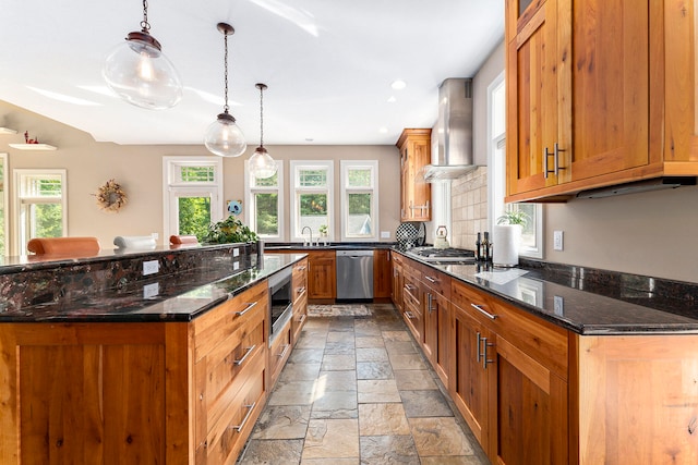 kitchen featuring stainless steel appliances, wall chimney range hood, light tile patterned floors, dark stone countertops, and hanging light fixtures