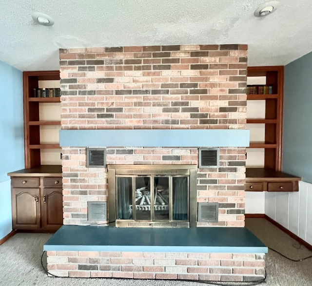 interior details featuring a fireplace, a textured ceiling, carpet flooring, and built in shelves