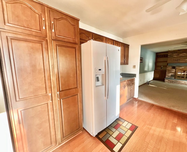 kitchen featuring white refrigerator with ice dispenser, light hardwood / wood-style flooring, a brick fireplace, and ceiling fan