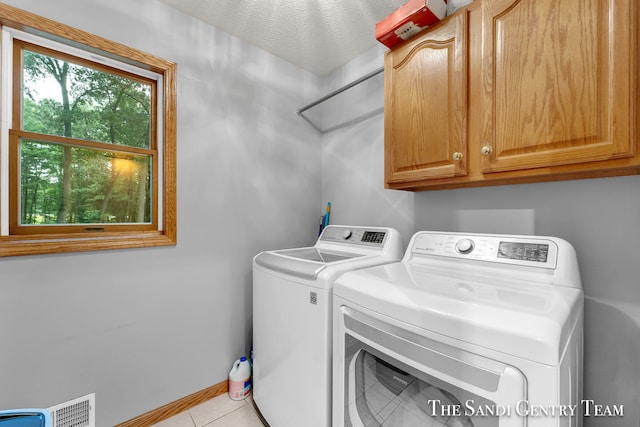 clothes washing area with cabinets, light tile patterned floors, washing machine and dryer, and a textured ceiling