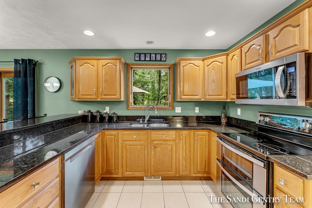 kitchen featuring light tile patterned flooring, sink, stainless steel appliances, and dark stone counters