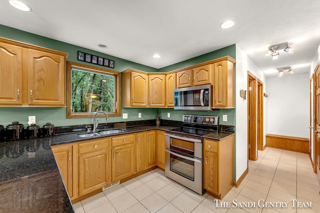 kitchen with light tile patterned floors, sink, appliances with stainless steel finishes, and dark stone counters