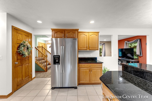 kitchen with stainless steel refrigerator with ice dispenser, a textured ceiling, dark stone counters, and light tile patterned flooring