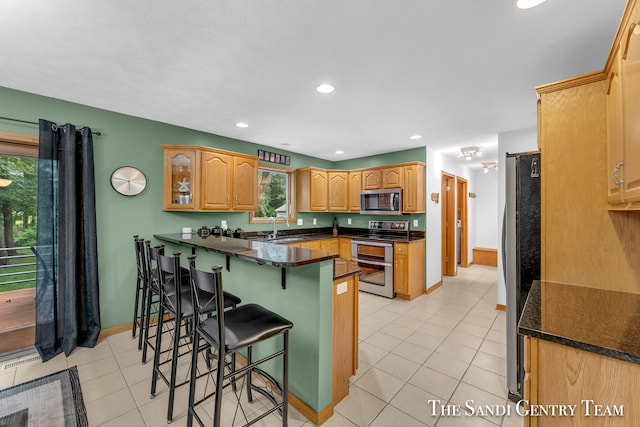 kitchen featuring sink, kitchen peninsula, a breakfast bar area, light tile patterned floors, and appliances with stainless steel finishes