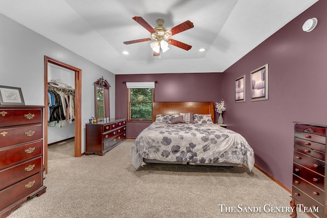 bedroom with light carpet, a walk in closet, a raised ceiling, ceiling fan, and a closet