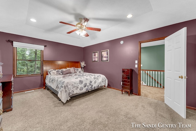 carpeted bedroom with ceiling fan and a raised ceiling