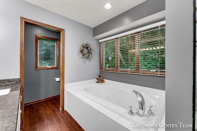 bathroom with vanity, a relaxing tiled tub, wood-type flooring, and a textured ceiling