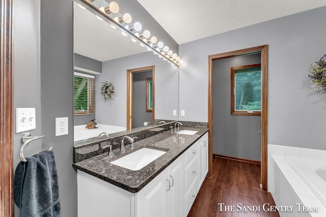 bathroom with hardwood / wood-style floors, vanity, and tiled tub