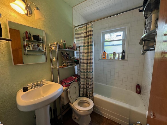 bathroom with a sink, toilet, shower / tub combo, and a textured wall