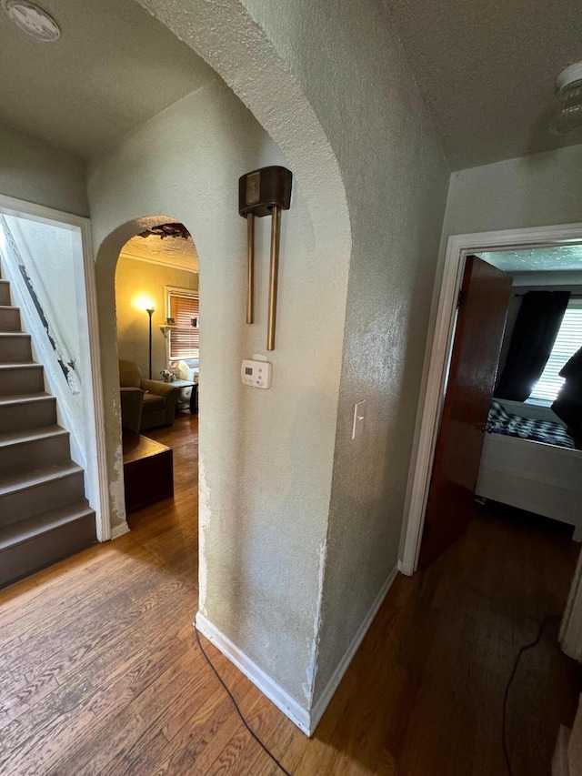 hallway with baseboards, arched walkways, wood finished floors, and stairway