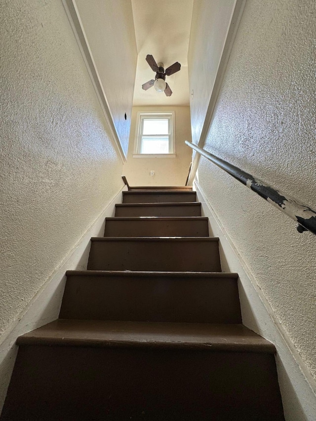 staircase with a ceiling fan and a textured wall