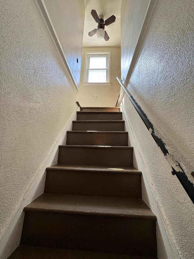 staircase featuring ceiling fan and a textured wall