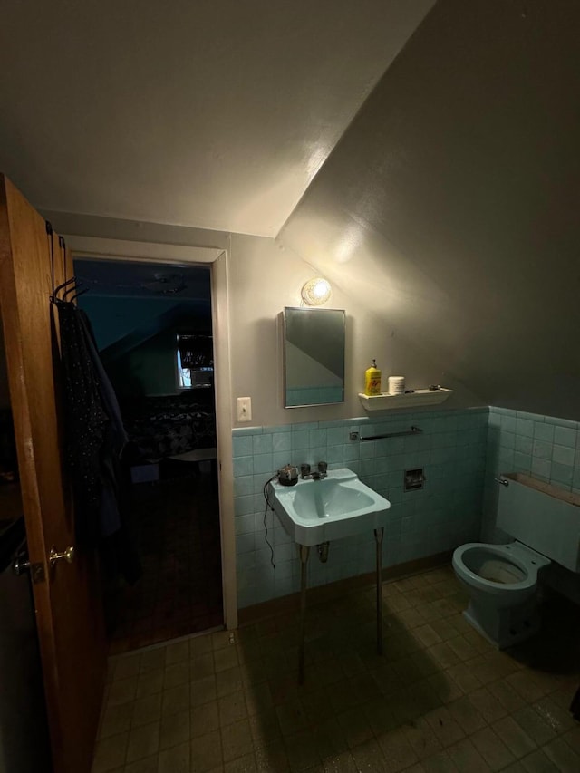 bathroom with toilet, tile walls, tile patterned floors, sink, and lofted ceiling