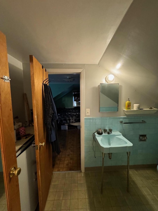 bathroom featuring a sink, a wainscoted wall, lofted ceiling, and tile walls