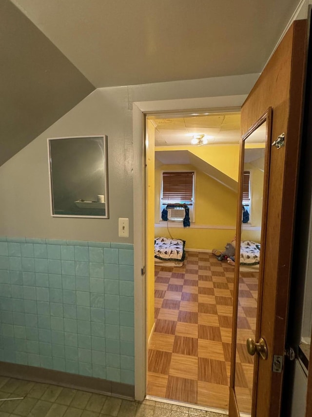 corridor with wainscoting, tile walls, and lofted ceiling