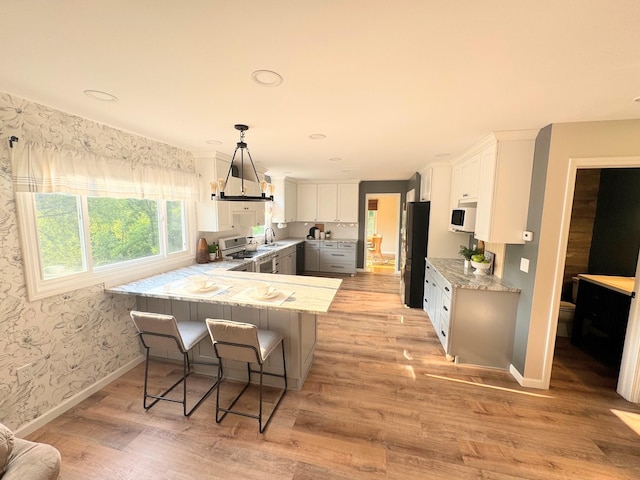 kitchen featuring light stone counters, white cabinets, light wood-type flooring, and black fridge