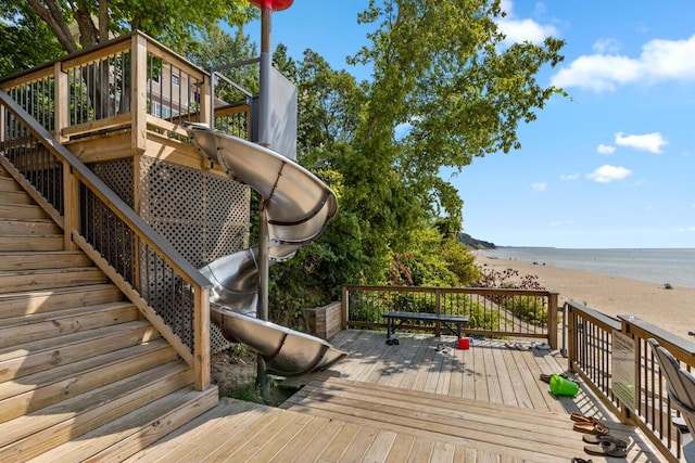 wooden terrace featuring a beach view, stairs, and a water view