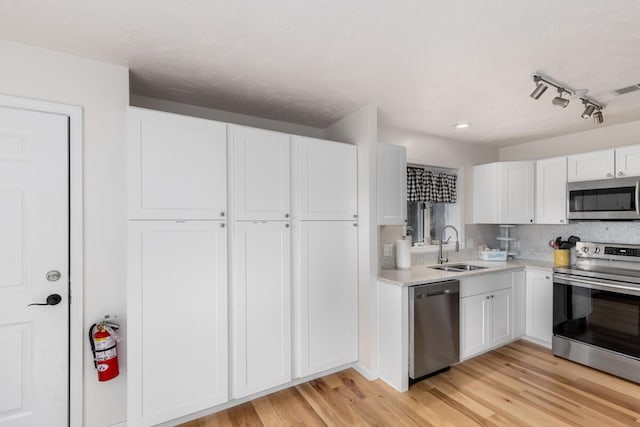 kitchen with light wood-type flooring, a sink, appliances with stainless steel finishes, white cabinets, and light countertops