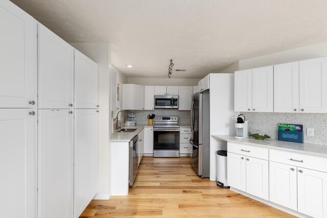 kitchen with light wood-style flooring, a sink, stainless steel appliances, white cabinetry, and backsplash