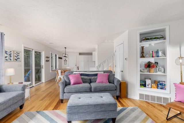 living area featuring built in shelves, visible vents, baseboards, stairs, and light wood-style floors