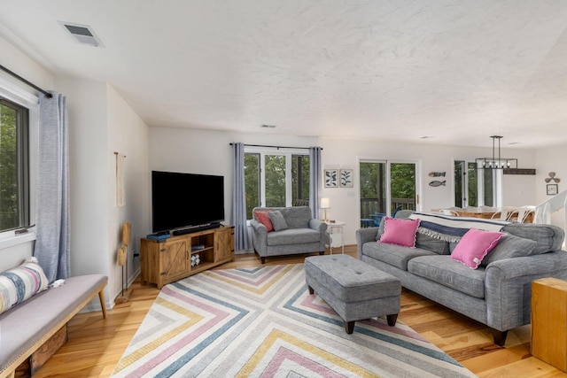 living area with light wood-style flooring, a notable chandelier, visible vents, and a textured ceiling