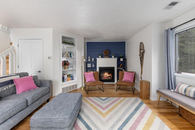 living room featuring visible vents, built in shelves, a glass covered fireplace, and wood finished floors