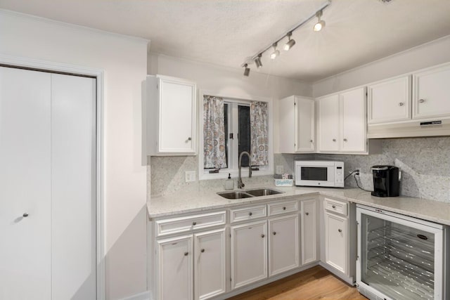 kitchen with white microwave, light wood finished floors, a sink, wine cooler, and white cabinets