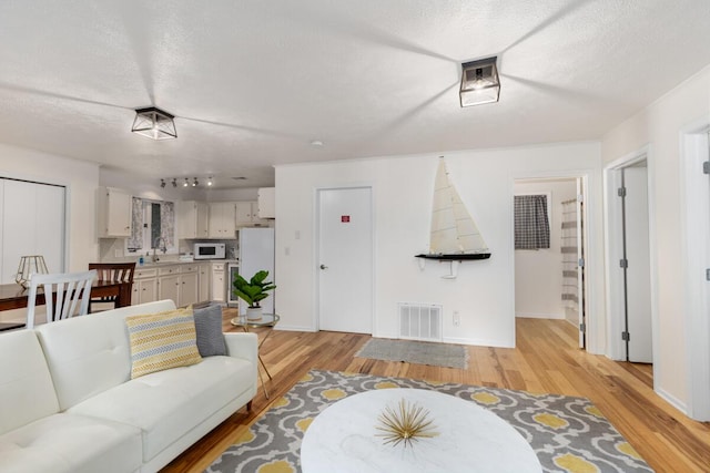 living area with visible vents, baseboards, light wood-style floors, and a textured ceiling