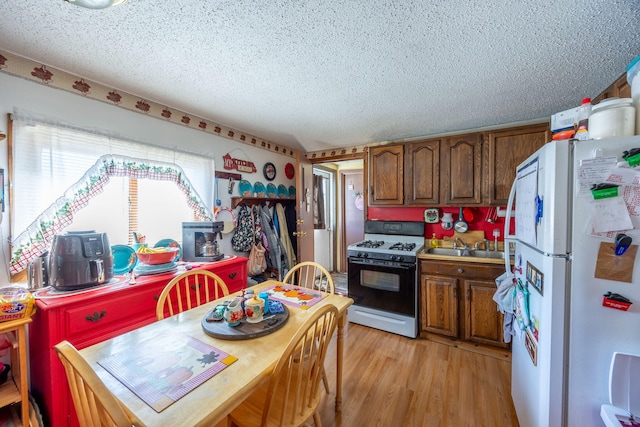 kitchen featuring light wood-style flooring, freestanding refrigerator, gas range oven, light countertops, and a textured ceiling