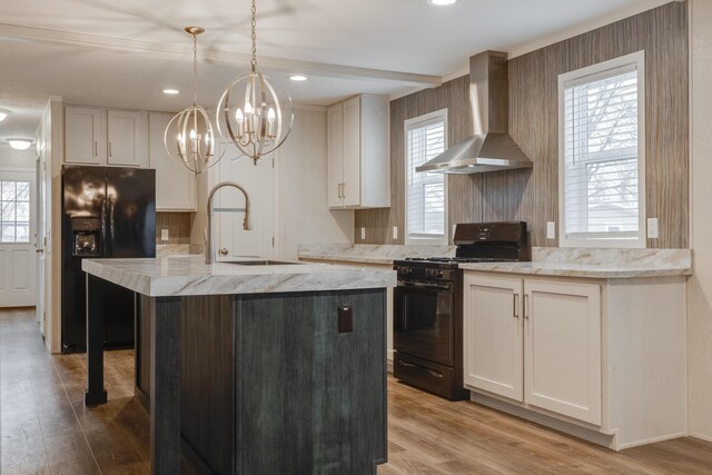 kitchen featuring an island with sink, plenty of natural light, black appliances, light hardwood / wood-style flooring, and wall chimney exhaust hood