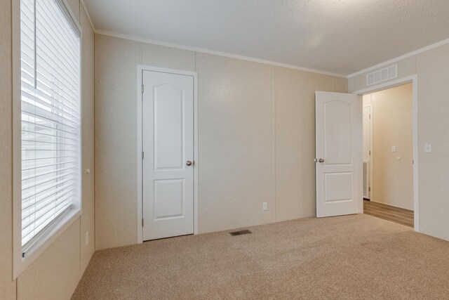 unfurnished room featuring light carpet, a textured ceiling, and ornamental molding