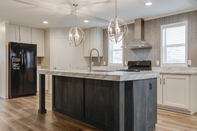 kitchen featuring wall chimney range hood, stove, black fridge, light hardwood / wood-style floors, and sink