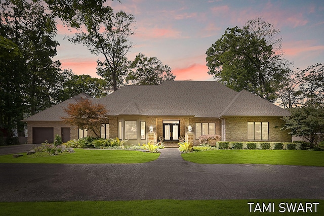 view of front of house featuring brick siding, roof with shingles, a lawn, a garage, and driveway