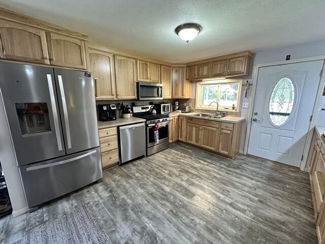 kitchen featuring a textured ceiling, light brown cabinets, hardwood / wood-style flooring, stainless steel appliances, and sink