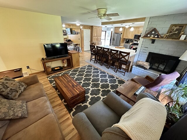 living room with ceiling fan, light wood-type flooring, and a brick fireplace