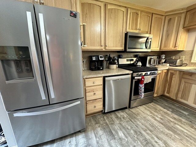 kitchen with appliances with stainless steel finishes, backsplash, light brown cabinets, and light hardwood / wood-style floors