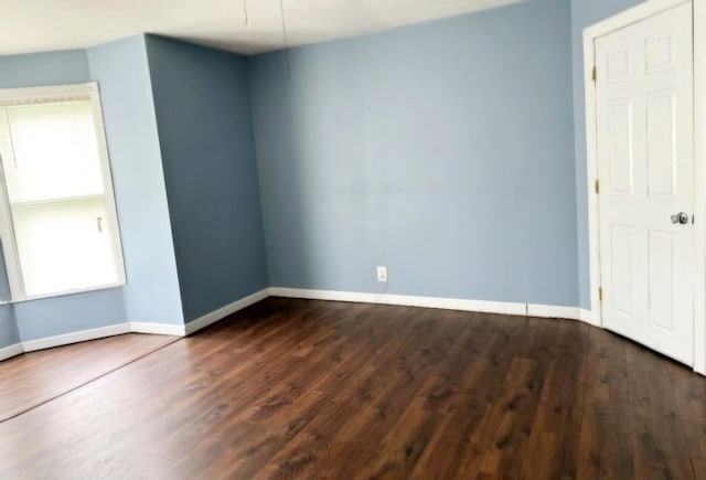 spare room featuring dark wood-type flooring and baseboards