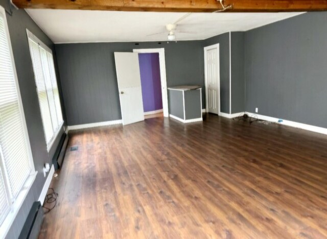 empty room featuring baseboards, baseboard heating, a healthy amount of sunlight, and wood finished floors