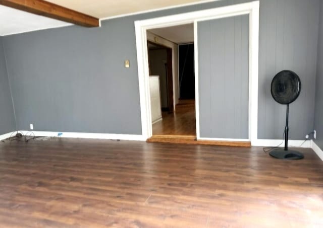 empty room featuring baseboards, beam ceiling, and wood finished floors