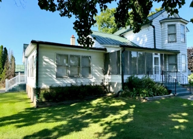 view of front of home featuring metal roof, a chimney, a front lawn, and a sunroom