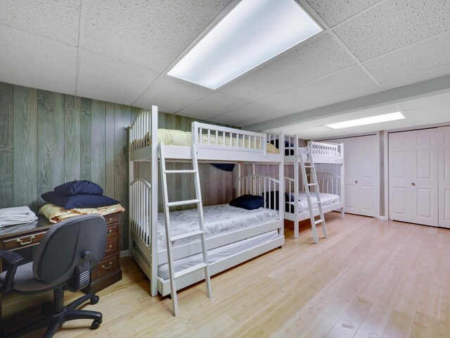 bedroom featuring light wood-type flooring, a paneled ceiling, and two closets