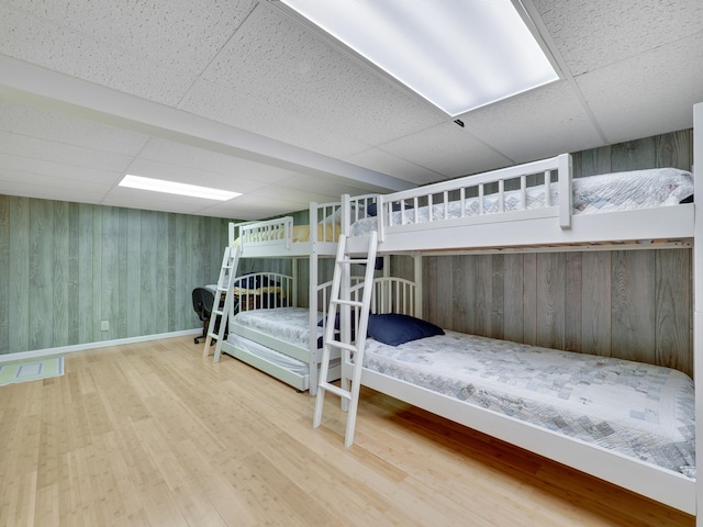 bedroom with wood walls, hardwood / wood-style flooring, and a drop ceiling