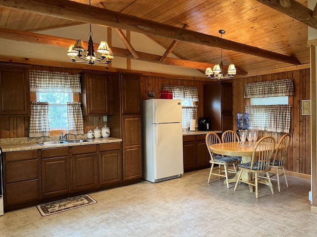 kitchen featuring an inviting chandelier, hanging light fixtures, white fridge, and wood walls