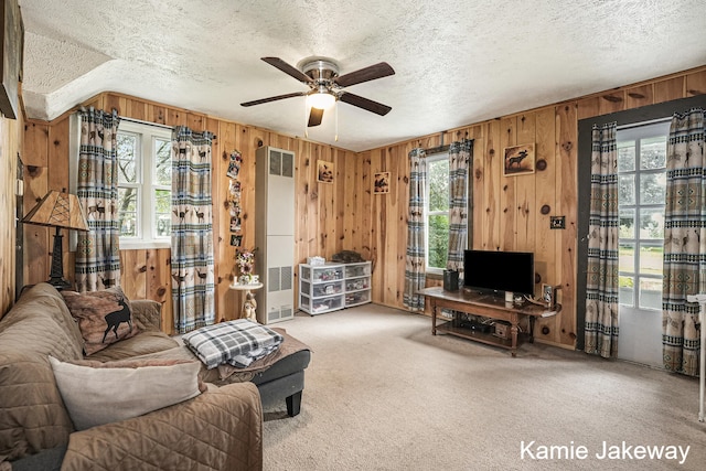 carpeted living room with ceiling fan, a textured ceiling, wooden walls, and a healthy amount of sunlight