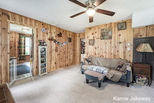 carpeted living room featuring ceiling fan, a textured ceiling, and wooden walls